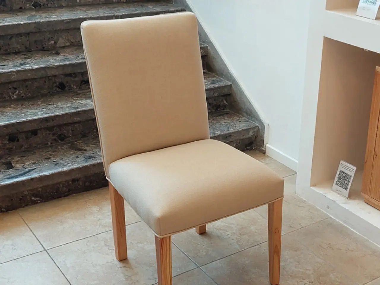 Silla de comedor con asiento y respaldo tapizados en ecocuero claro, junto a una escalera