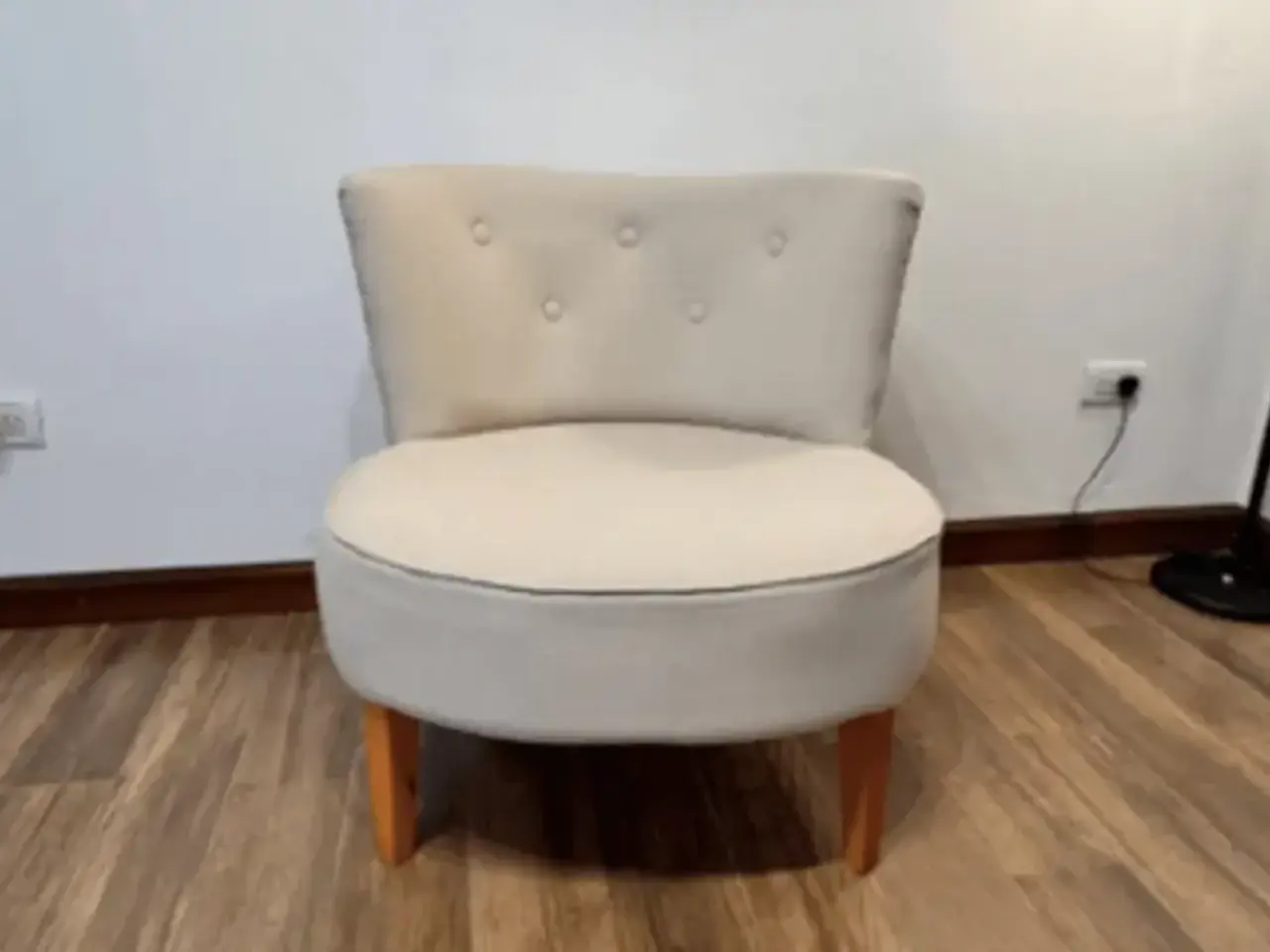 Butaca baja de asiento redondo tapizada en tela crema, con botones en el respaldo y patas de madera