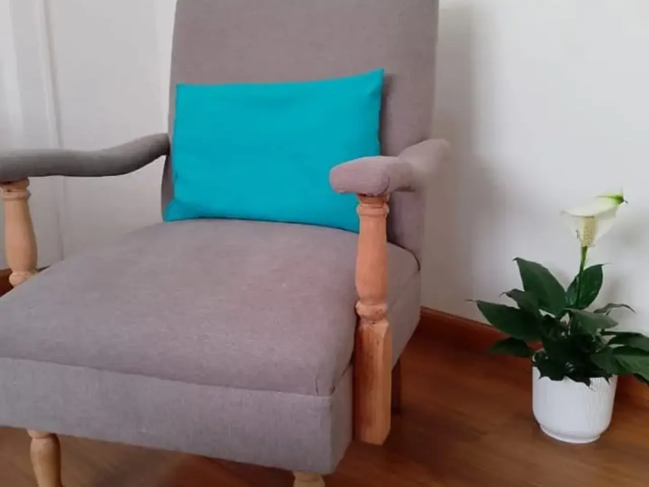 Butaca con brazos de madera torneada tapizada en tela gris, con un almohadón turquesa